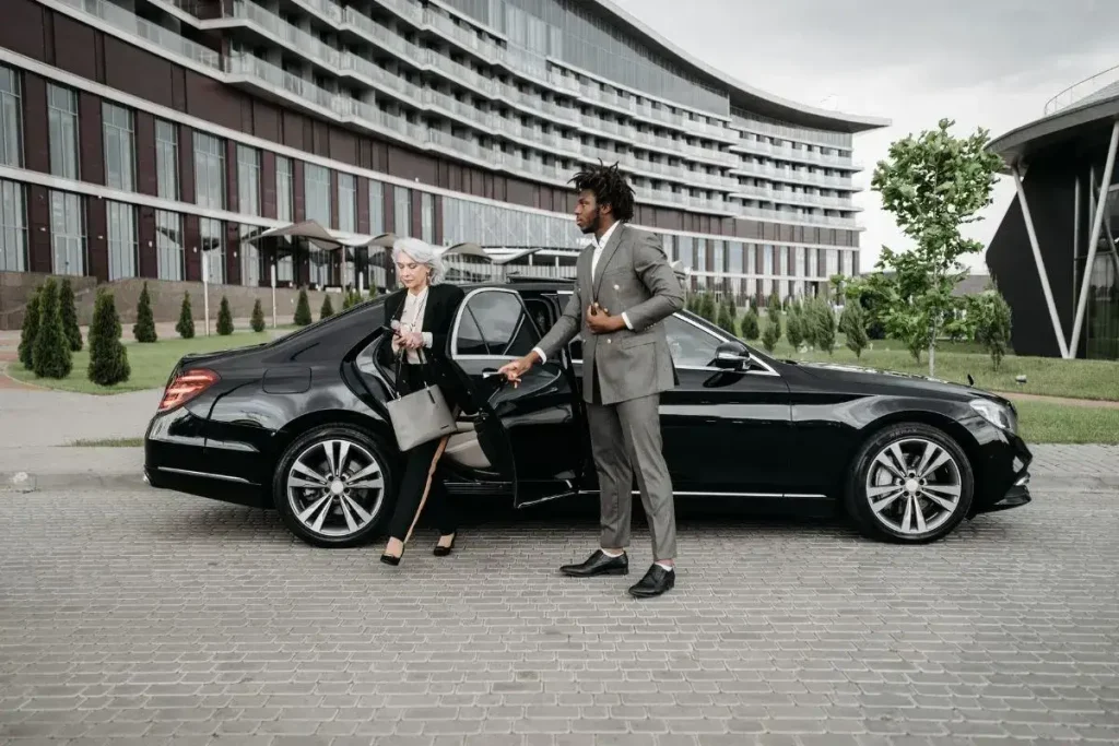 Chauffeur Limo Service Black Premium Limo Arrival Elegant woman stepping out of a black Mercedes-Benz S-Class sedan assisted by a professional chauffeur in a suit, highlighting premium chauffeur limo service for executive arrival by Black Premium Limo.