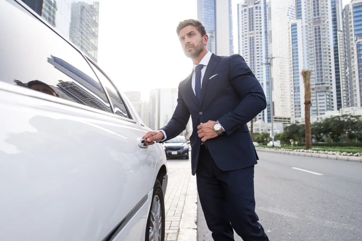 Guelph-Airport-Limo-Service-Luxury-Transportation Professional chauffeur in a navy suit opening a white luxury car door for Guelph Airport Limo Service.